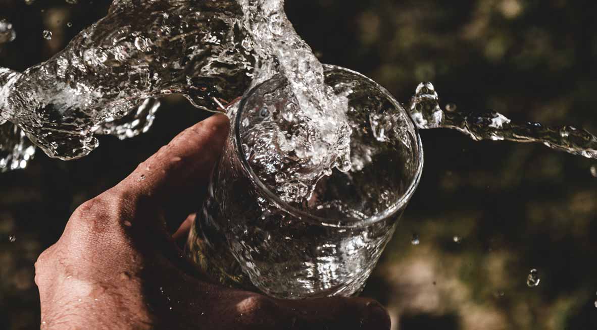 Eine Hand hält ein Glas, in das Wasser fließt.