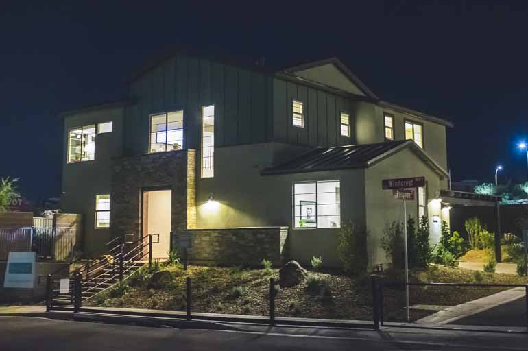 Ein großes Einfamilienhaus bei Nacht, in dem in den Zimmern und vor dem Haus Licht brennt