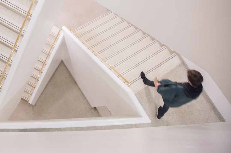 Ein Mensch geht in einem weißen Treppenhaus die Treppen herunter