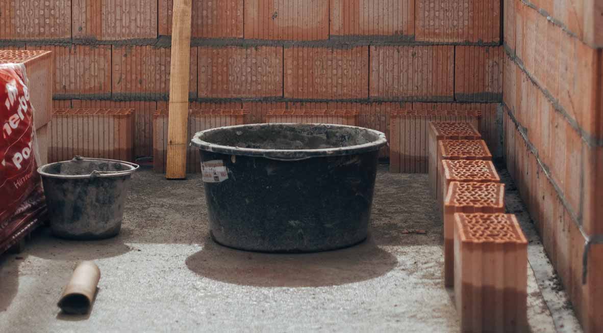 Baustelle mit Eimer und Backsteinen, auf der ein neues Haus gebaut wird.