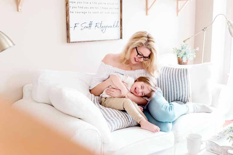 Eine Frau albert lachend mit ihrem kleinen Kind auf einem Sofa herum.