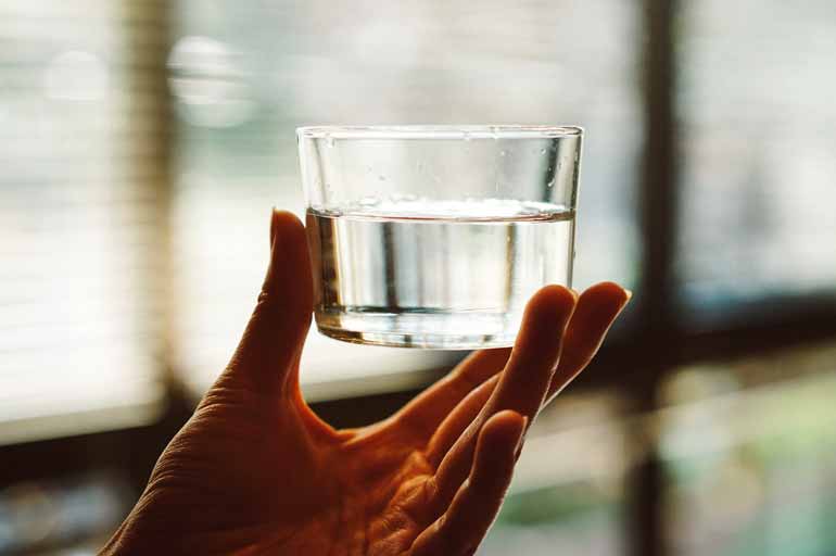 Eine Hand hält ein Glas Trinkwasser.
