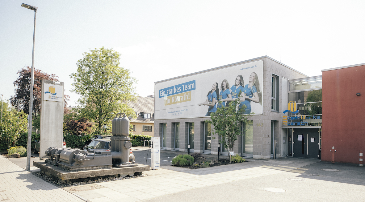 Außenaufnahme des Firmengebäudes der StadtWerke Rösrath. An der Hauswand hängt ein großer Banner mit dem Logo und vier Damen aus dem Kundenzentrum.