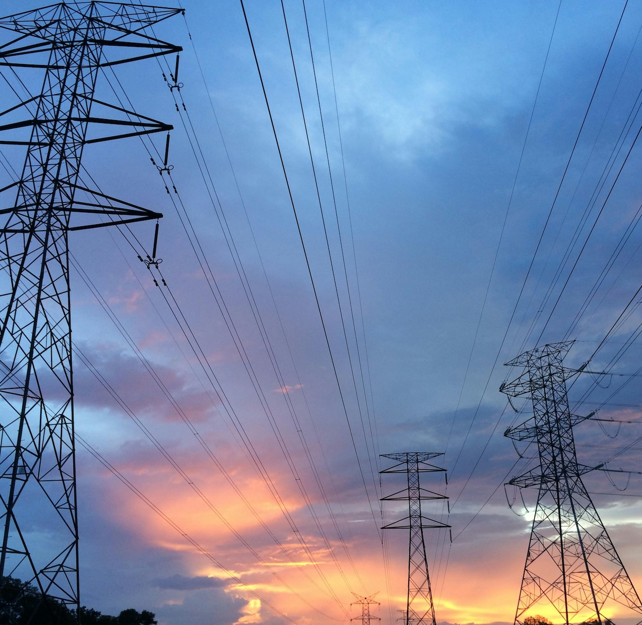 Drei Strommasten mit Stromleitungen mit einem spannenden Himmel voller Wolken und untergehender Sonne